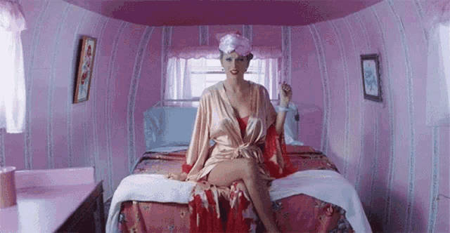 a woman is sitting on a bed in a pink room wearing a robe and smoking a cigarette .