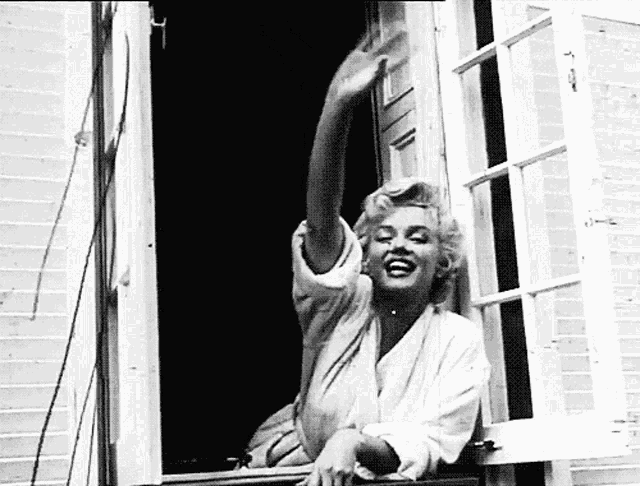 a black and white photo of a woman looking out a window