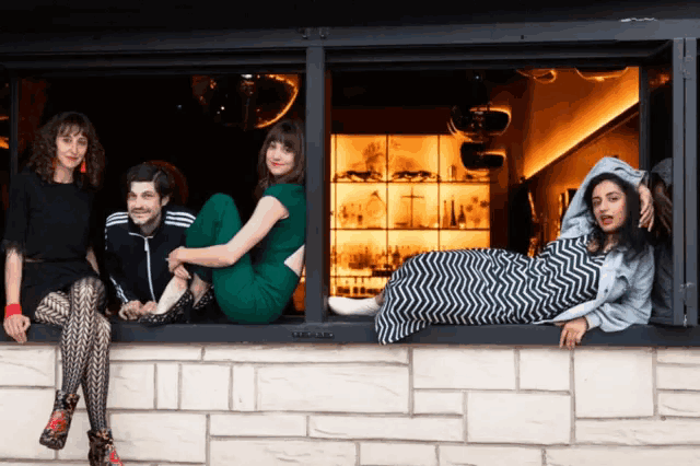 four people are sitting on a window sill in front of a bar