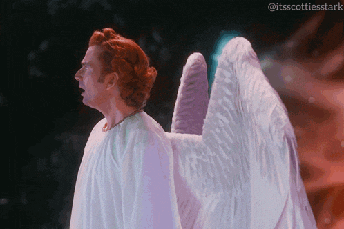 a man in a white robe with angel wings stands in front of a dark background