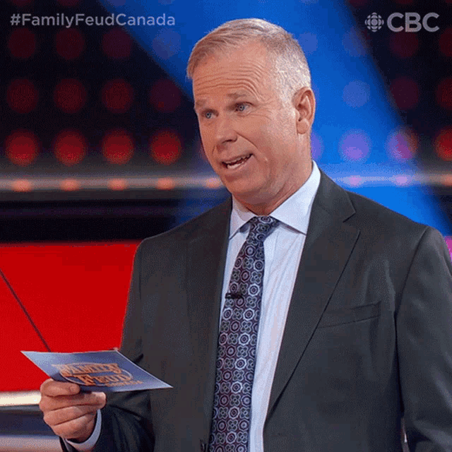 a man in a suit and tie is holding a piece of paper that says " family feud canada "