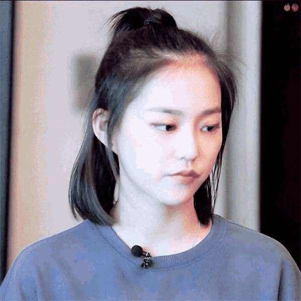 a woman wearing a blue shirt and a ponytail looks at the camera