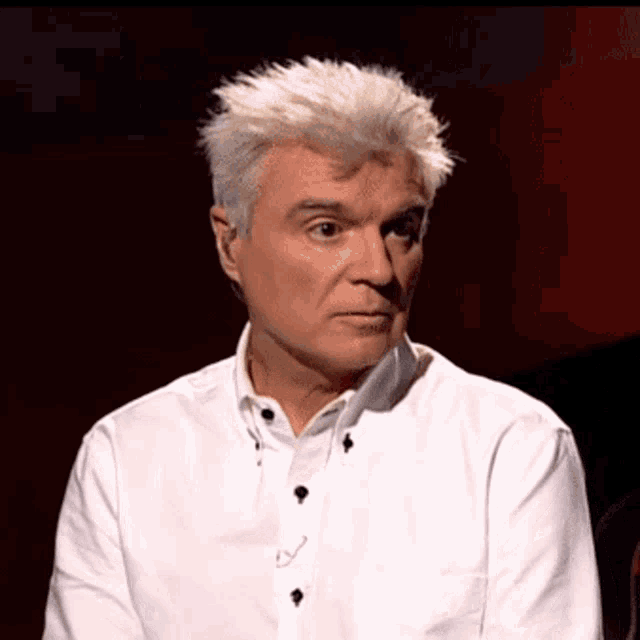 a man in a white shirt with black buttons is looking at the camera