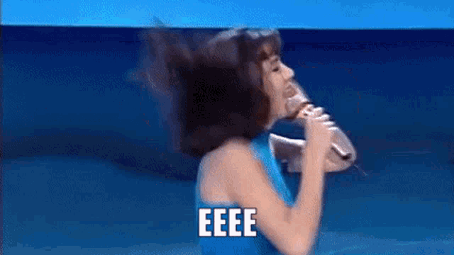 a woman in a blue dress is singing into a microphone with the words eeee written above her .