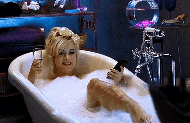 a woman is taking a bath in a tub while holding a glass of wine and a cell phone .