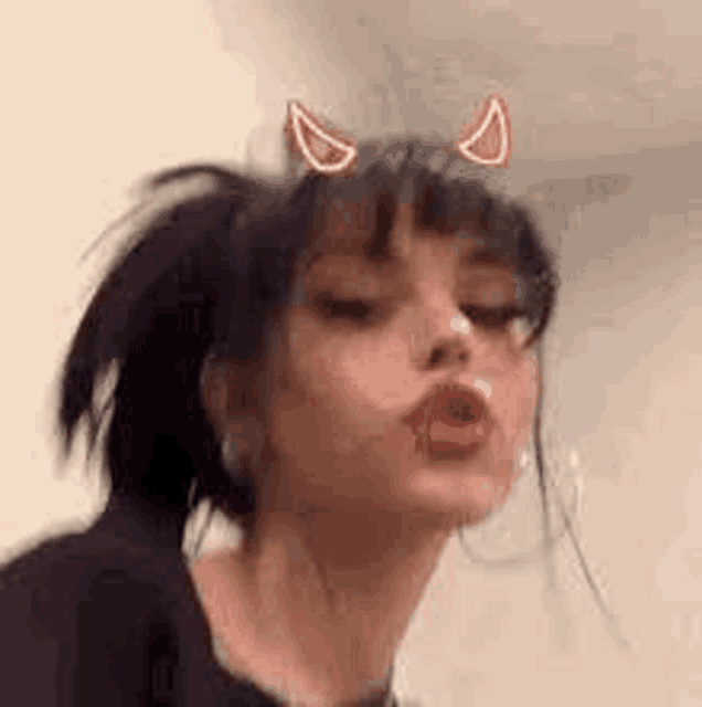 a girl with devil horns on her head is wearing a black shirt and earrings .