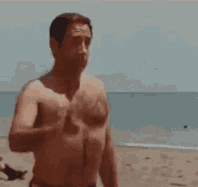 a man without a shirt is standing on a beach looking at the ocean .
