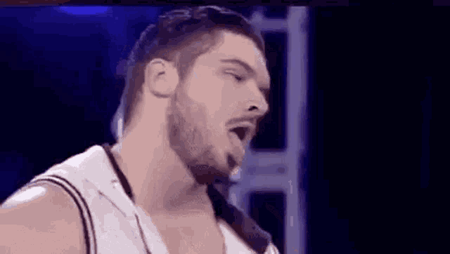 a man with a beard is standing in a dark room with his eyes closed and his tongue out .