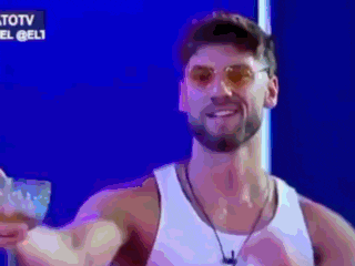 a man wearing sunglasses and a white tank top is smiling in front of a blue screen that says totv