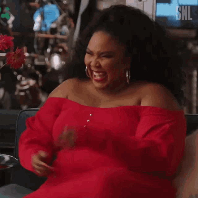 a woman in a red off the shoulder dress is laughing while sitting on a couch .
