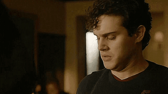 a young man with curly hair is wearing a black sweater and a red collar .