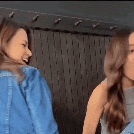 two women are standing next to each other in front of a wooden wall and laughing .