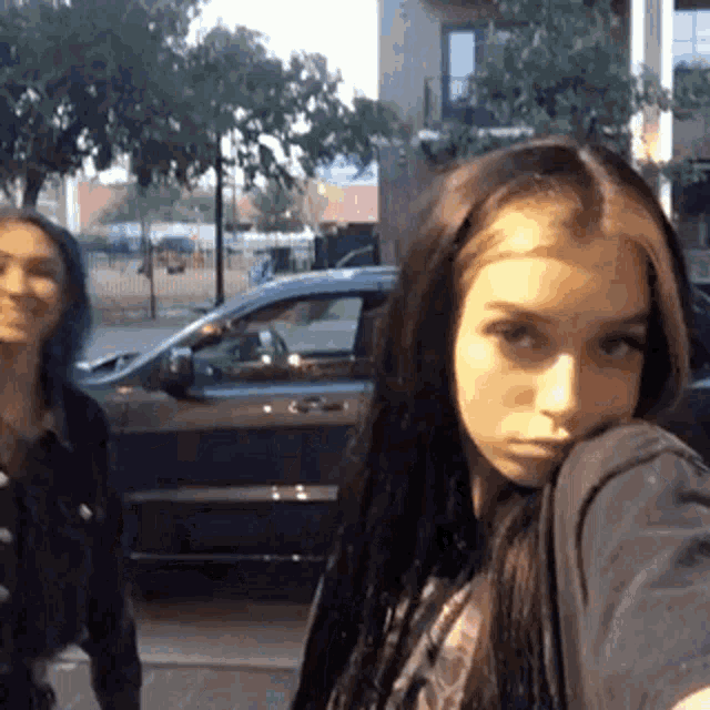 two girls are standing in front of a black car