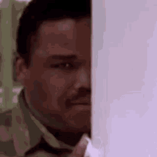 a man with a mustache is peeking out from behind a door .