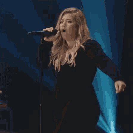 a woman is singing into a microphone on a stage and the word woah is on the screen .