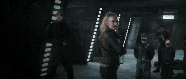 a woman with a gun stands in a dark room with other people