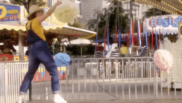 a woman in overalls is dancing in front of a carousel with a sign that says ' cotton candy ' on it