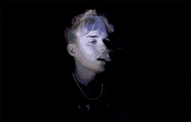 a man with rainbow hair is singing into a microphone in a dark room .