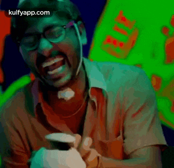 a man wearing glasses is laughing while holding a cell phone .