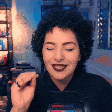 a woman with curly hair and a nose ring is smiling with her eyes closed and holding something in her hand