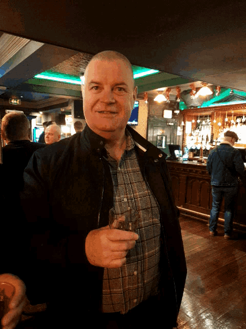 a man in a plaid shirt holds a glass of wine in a bar