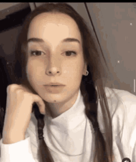 a young woman with braids in her hair is wearing a white turtleneck sweater and earrings .