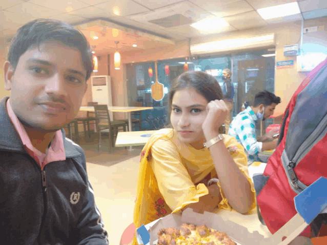 a man and a woman are sitting at a table with a pizza box in front of them