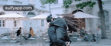 a man is carrying a woman in his arms in front of a restaurant with umbrellas .