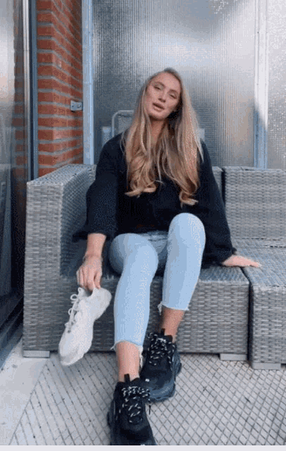a woman is sitting on a wicker chair holding a pair of sneakers