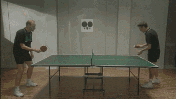 two men are playing ping pong in a room with two ping pong balls on the wall