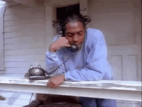 a man in a blue sweatshirt is talking on a telephone while sitting on a porch .