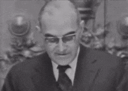 a man wearing glasses and a suit and tie is talking
