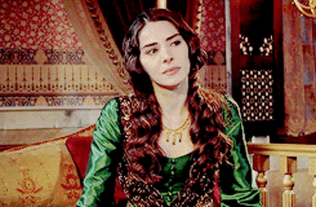 a woman in a green dress and necklace is sitting on a couch