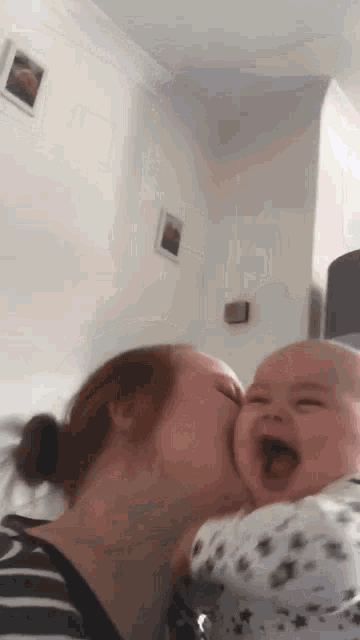 a woman is kissing a baby who is laughing with his mouth open