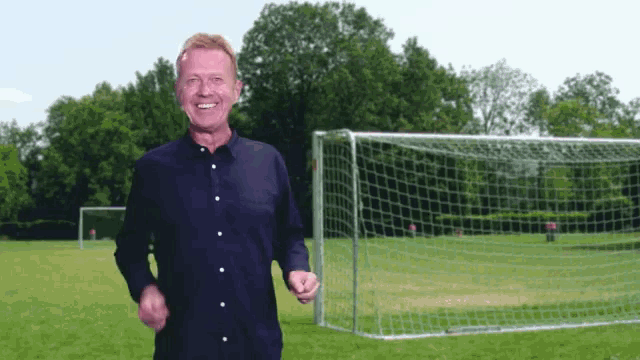 a man in a black shirt stands in front of a soccer goal on a field