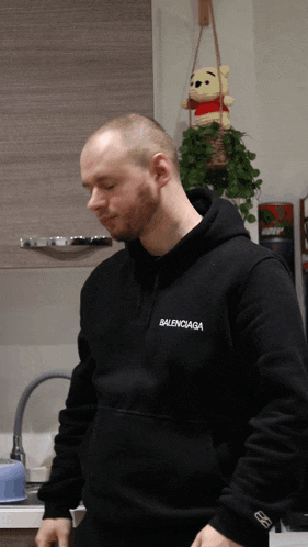 a man wearing a black balenciaga hoodie stands in front of a winnie the pooh stuffed animal