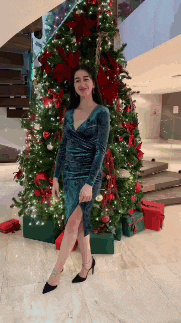 a woman in a blue dress is standing in front of a christmas tree .
