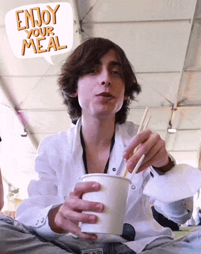 a young man is eating noodles with chopsticks and a speech bubble says enjoy your meal