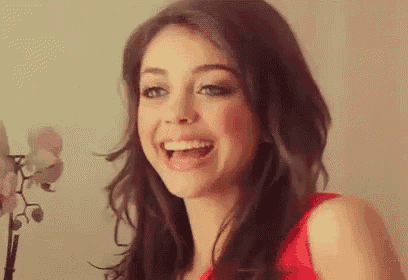 a woman in a red dress is smiling with her mouth open and a flower in the background .