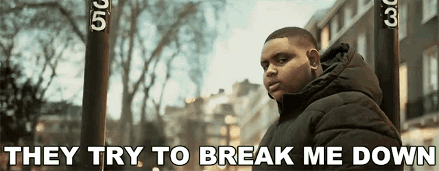 a man in a black jacket stands in front of a sign that says " they try to break me down "