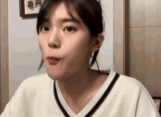 a woman in a white sweater is making a funny face while looking at the camera .