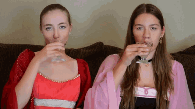 two women drinking from glasses one in a red and one in a pink dress