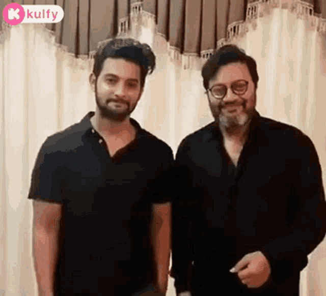 two men are standing next to each other in front of a white curtain and smiling .