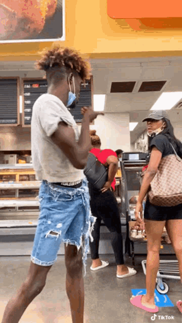 a man wearing a mask and shorts is standing in a grocery store talking to a woman