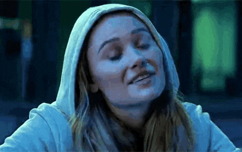a woman wearing a hoodie is smiling with her eyes closed in a dark room .