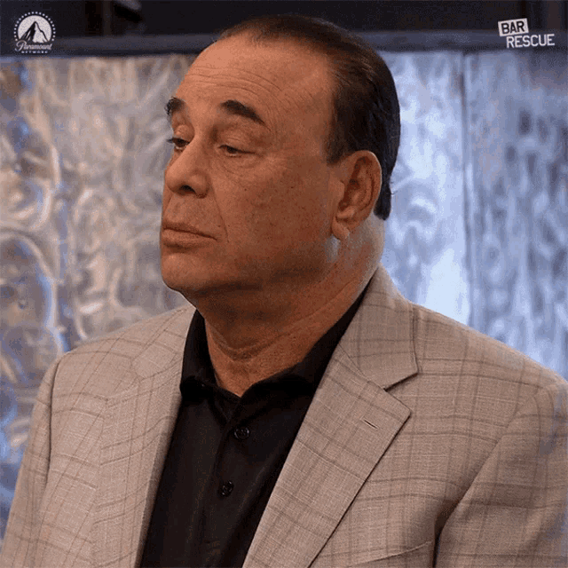 a man wearing a suit and a black shirt is standing in front of a sign that says " bar rescue "