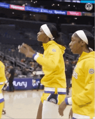 two female basketball players wearing yellow uniforms are standing on a court