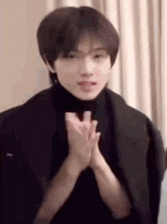 a young man in a black turtleneck is clapping his hands together .