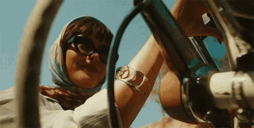 a woman wearing sunglasses and a scarf is looking through the steering wheel of a vehicle