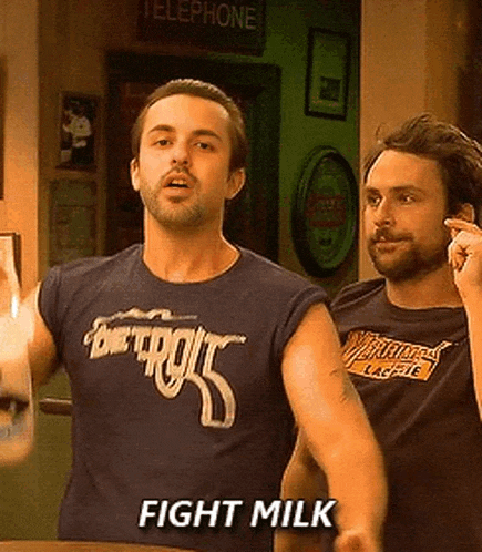 two men are standing next to each other in a bar and one of them is wearing a t-shirt that says fight milk .